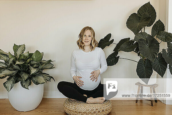 Schwangere Frau sitzt im Schneidersitz auf einem Hocker zu Hause