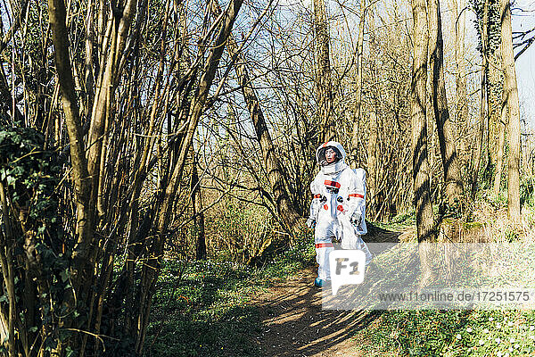 Young female explorer with space suit and helmet walking on forest path
