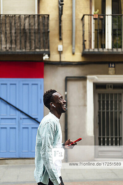 Junger Mann mit Smartphone und In-Ear-Kopfhörern auf der Straße