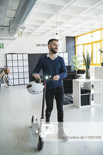 Smiling male professional wheeling push scooter while walking at coworking office