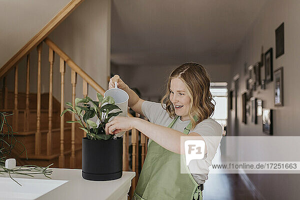 Aufgeregte schwangere Frau beim Gießen einer Topfpflanze zu Hause