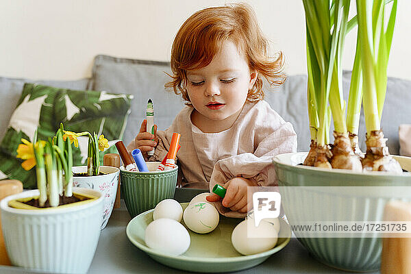Nettes Mädchen  das Eier in einem Teller mit einer Topfpflanze während der Osterzeit betrachtet