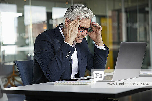 Mature businessman sitting with head in hands in office