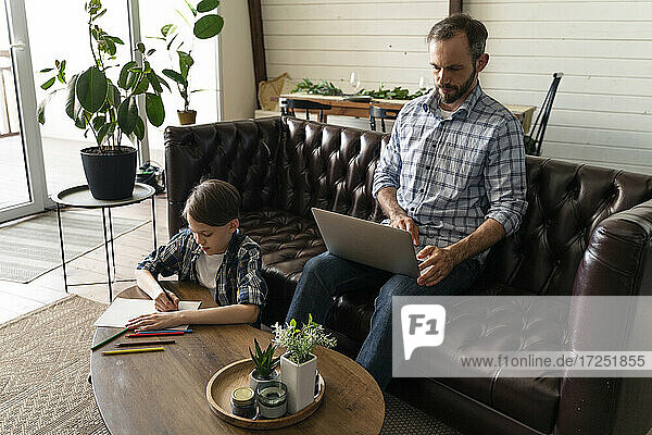 Father using laptop while son drawing at home