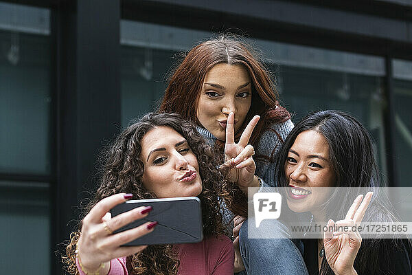 Junge Frau schmiegt sich an  während sie mit Freunden ein Selfie auf dem Handy macht
