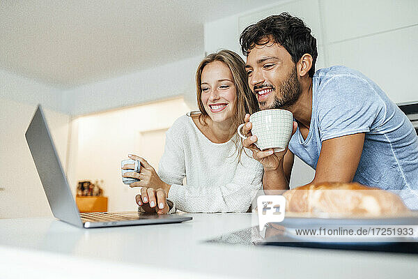 Young couple using laptop in kitchen at home