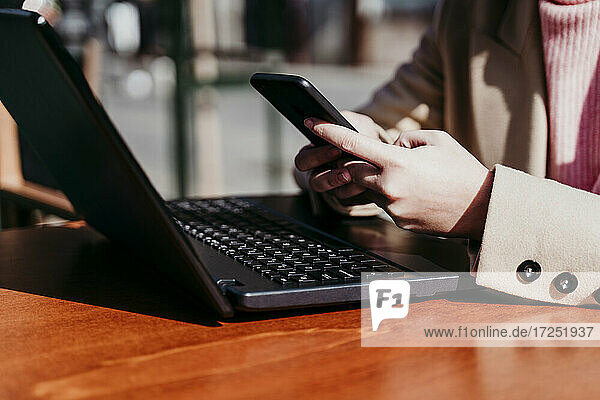 Frau benutzt Mobiltelefon mit Laptop in einem Straßencafé
