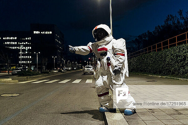 Weibliche Astronautin im Raumanzug  die nachts auf dem Gehweg in der Nähe der Straße steht