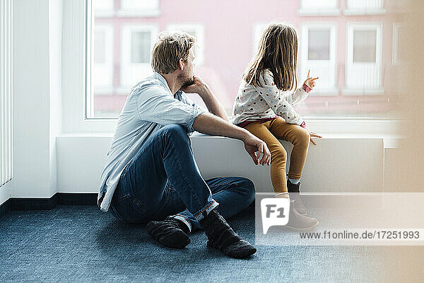 Father and daughter looking through window at home