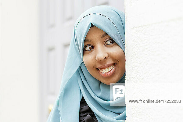 Lächelnde Frau mit Hidschab  die um die Mauer lugt