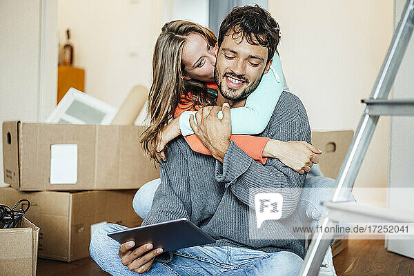 Young woman kissing boyfriend using digital tablet at home
