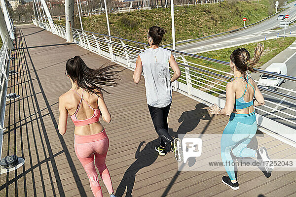 Multi ethnic male and female friends running on bridge during sunny day