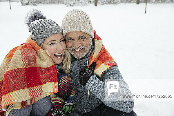 Smiling couple wrapped in blanket during winter