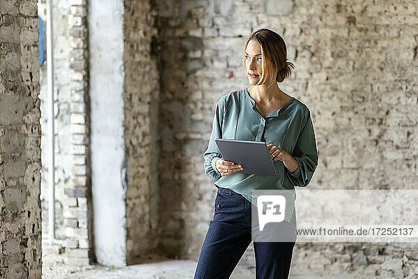 Architektin schaut weg  während sie ein digitales Tablet auf einer Baustelle hält