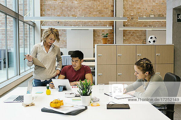 Eine Unternehmerin unterstützt einen jungen männlichen Mitarbeiter bei einer Besprechung im Büro