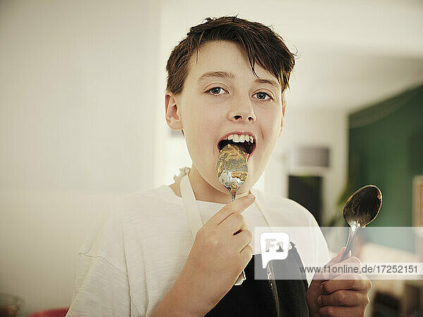 Junge leckt Muffinteig am Löffel in der Küche