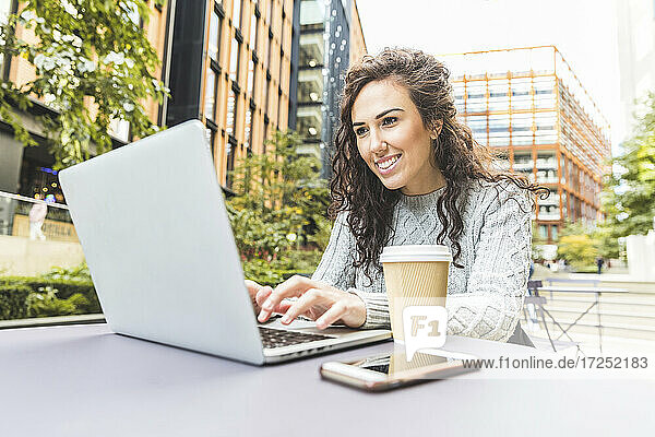 Lächelnde Geschäftsfrau mit Laptop in einem Café in der Stadt