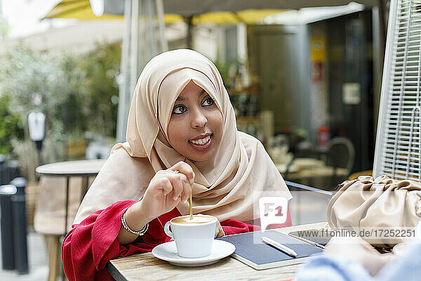 Smiling young woman stirring coffee while sitting at sidewalk cafe