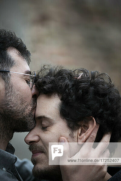 Mature man kissing male friend on forehead outdoors