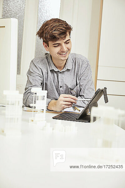 Smiling male architect working on digital tablet while sitting at office