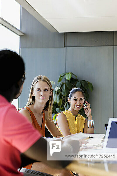 Unternehmerin  die mit einem Handy telefoniert  während sie mit einem Kollegen in einer Besprechung sitzt