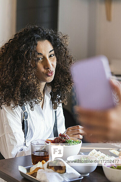 Eine Freundin fotografiert eine junge Frau  die in einem Restaurant beim Essen sitzt