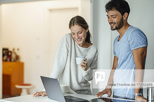 Glückliche Frau schaut auf einen Laptop  während sie bei ihrem Freund zu Hause steht