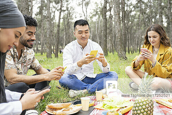Männliche und weibliche Freunde benutzen ihr Smartphone während einer Party im Wald