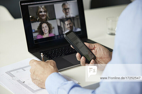 Geschäftsmann  der ein Mobiltelefon benutzt  während er an einer Besprechung mit einem Kollegen im Büro teilnimmt