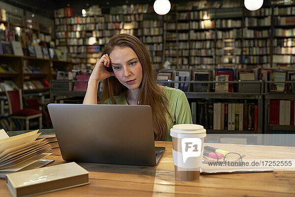 Junge Frau studiert in einer Bibliothek mit Laptop
