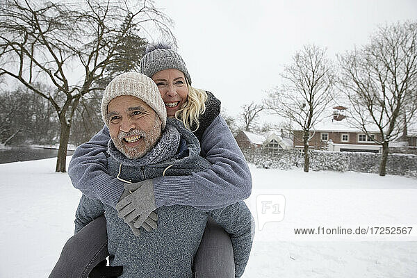 Älterer Mann nimmt Frau im Winter im Park huckepack
