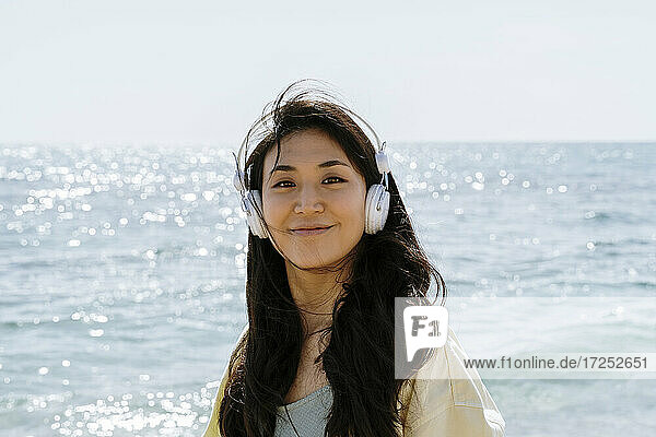 Schöne Frau mit In-Ear-Kopfhörern steht am Strand während des sonnigen Tages