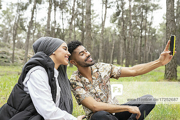 Smiling woman with young man taking selfie in forest