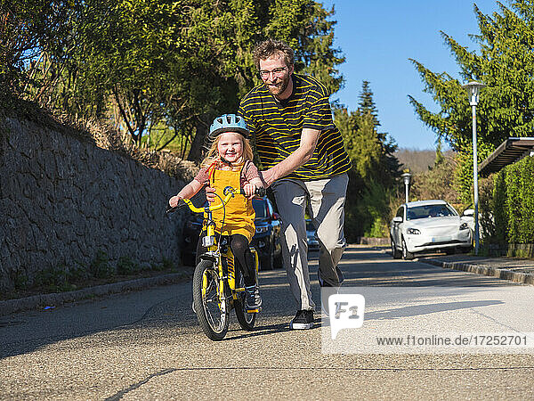 Smiling father assisting daughter while cycling on road