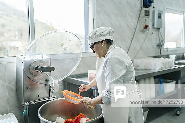 Weiblicher Käseexperte beim Einsatz eines Siebs in einer Fabrik