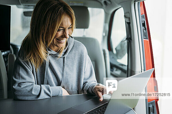 Lächelnde Geschäftsfrau  die in einem Lieferwagen an einem Laptop arbeitet