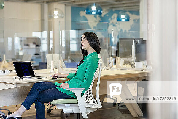 Female professional contemplating while sitting at desk in coworking office