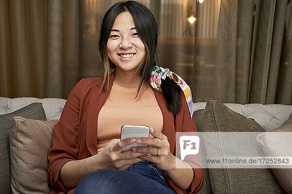 Lächelnde Frau mit Mobiltelefon auf dem Sofa in der Hotellobby