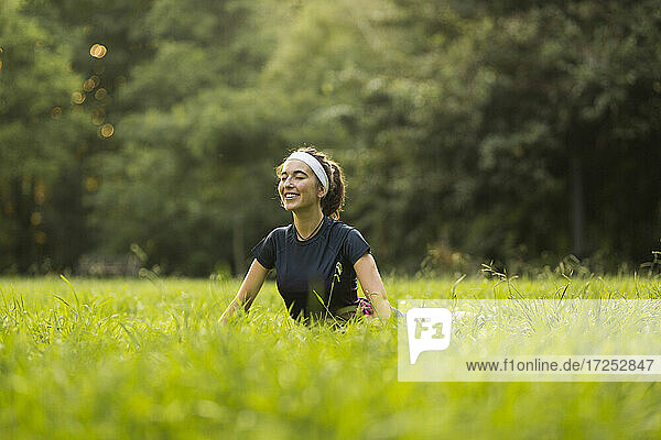 Lächelnde Frau übt Yoga auf Gras in einem öffentlichen Park