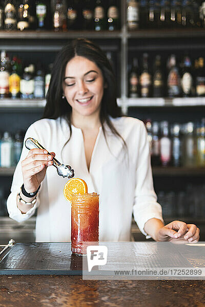Smiling female bartender serving cocktail at counter