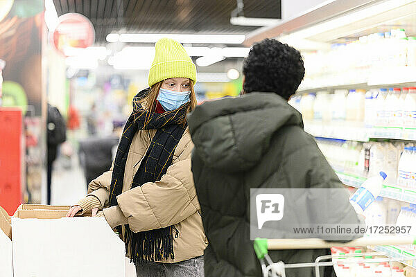 Female friends in warm clothing buying groceries at supermarket during COVID-19