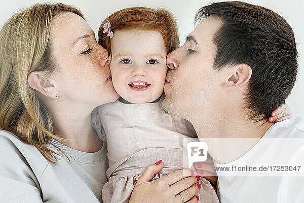 Mother and father kissing cute daughter at home