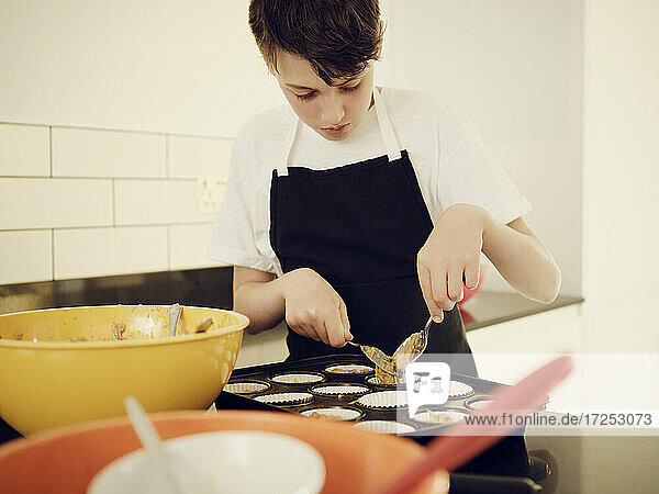 Junge füllt Muffinblech mit Teig in der Küche zu Hause
