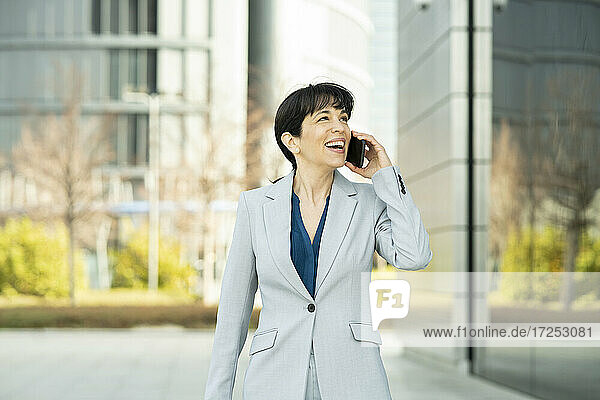 Lächelnde Geschäftsfrau  die in einem Büropark mit einem Mobiltelefon spricht