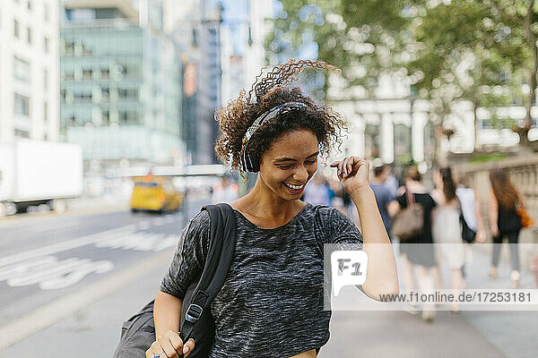 Glückliche Frau mit zerzaustem Haar hört Musik über Kopfhörer in der Stadt