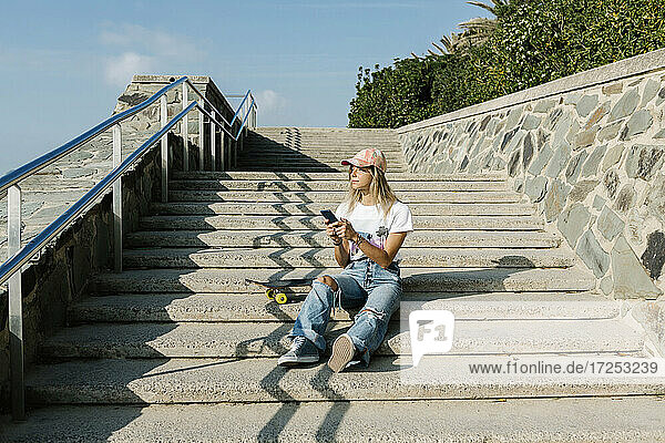 Mittlere erwachsene Frau mit Mobiltelefon  die auf einer Treppe sitzend an einem sonnigen Tag nachdenkt
