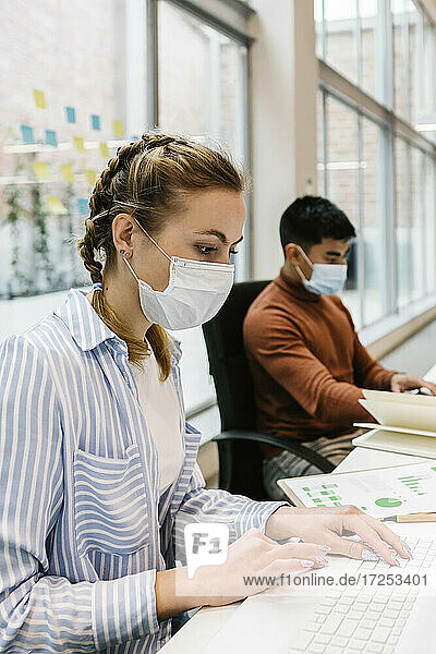 Weibliche Fachkraft nutzt Laptop eines männlichen Kollegen in einem Coworking-Büro während einer Pandemie