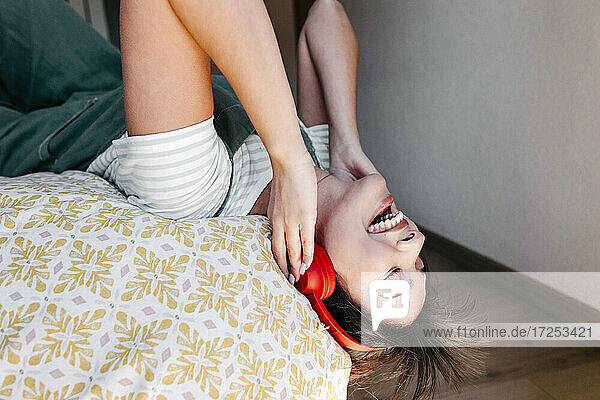 Glückliche Frau hört Musik über Kopfhörer  während sie auf dem Bett liegt