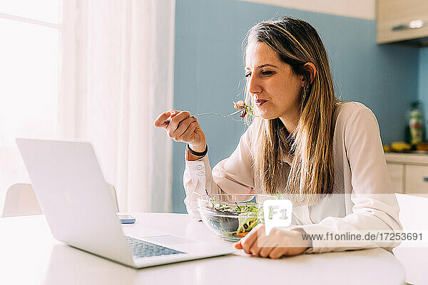 Italien  Frau isst Salat und schaut auf Laptop