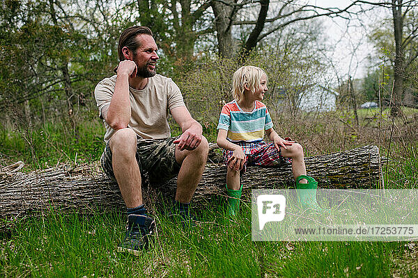 Canada  Ontario  Kingston  Father and son sitting on log in forest
